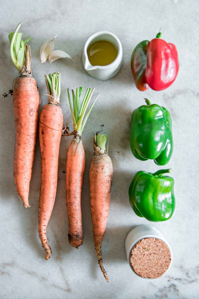 four carrots, three bell peppers, olive oil, and salt on a white table