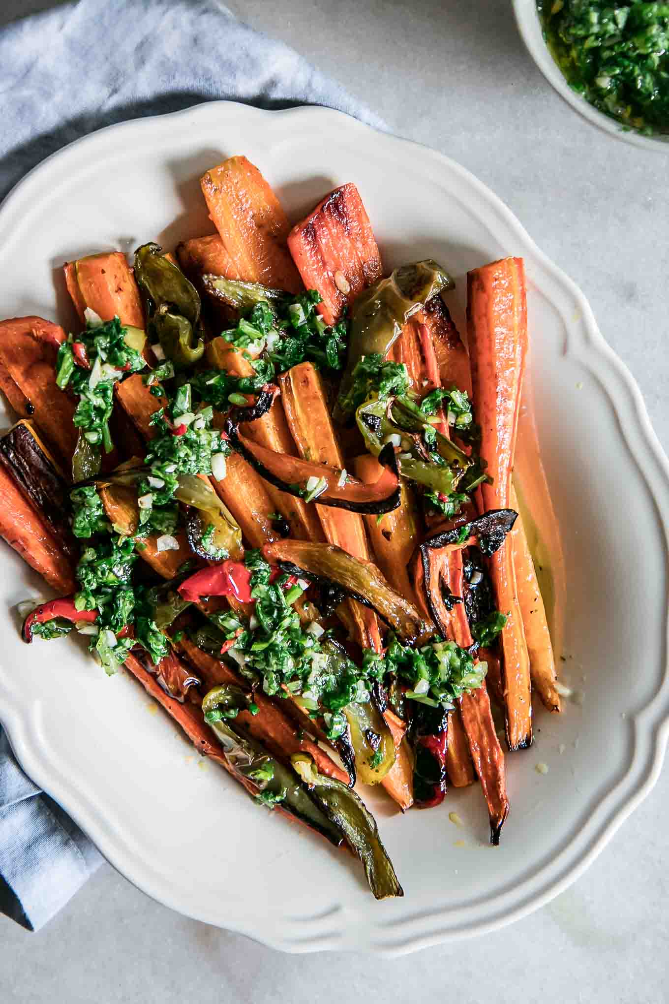 a white plate with roasted carrots and bell peppers on a white table with a blue napkin