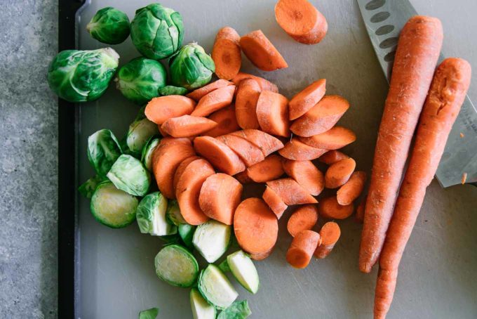 cut carrots and brussels sprouts on a white cutting board