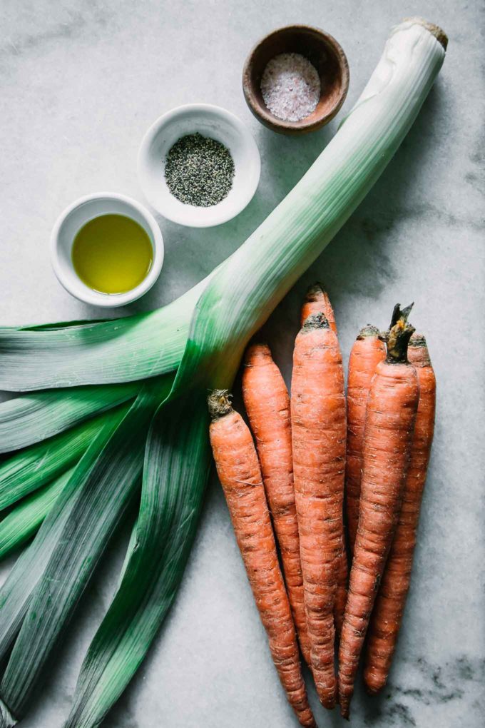 leeks, carrots, and bowls of oil, salt, and pepper on a white countertop