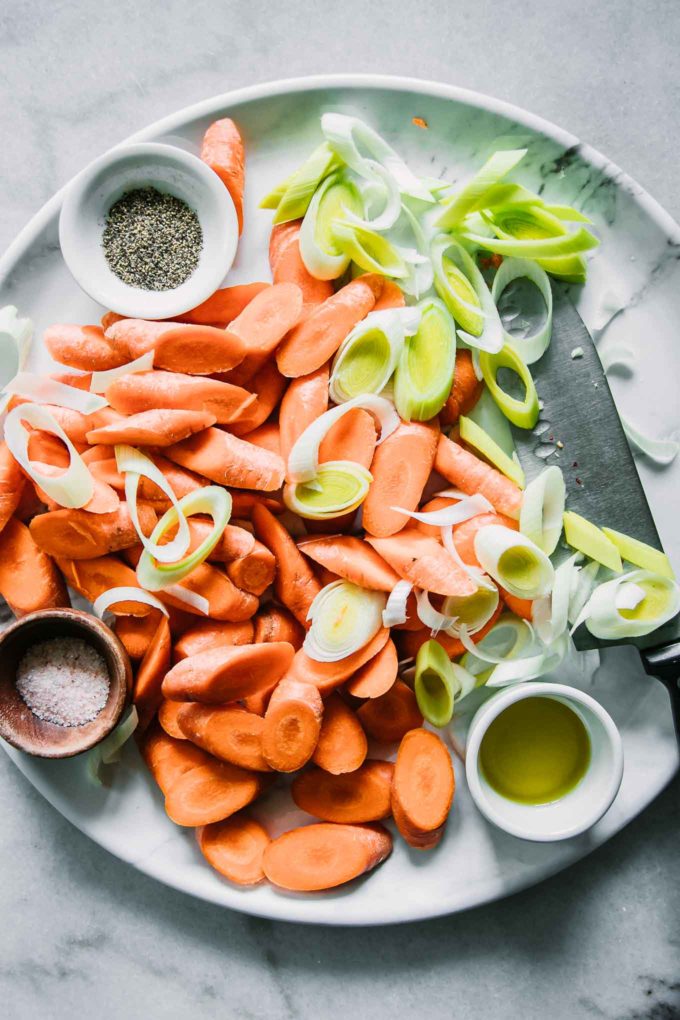 cut carrots and leeks on a white serving tray with bowls of oil, salt,and pepper