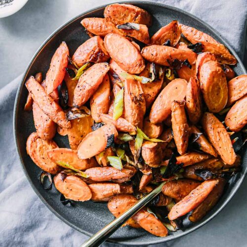 baked carrots and leeks on a blue plate on a white table with a gold fork