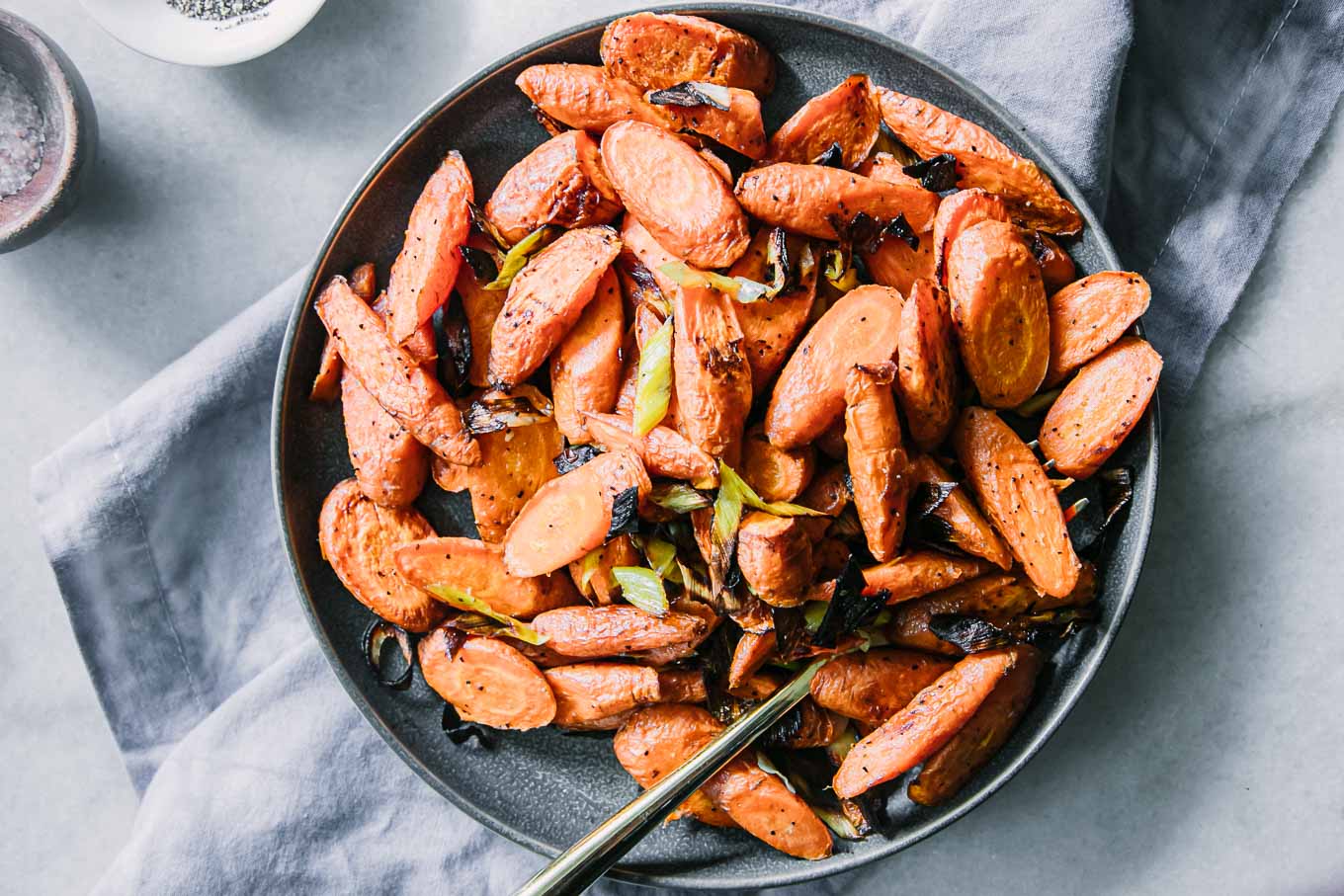baked carrots and leeks on a blue plate on a white table with a gold fork