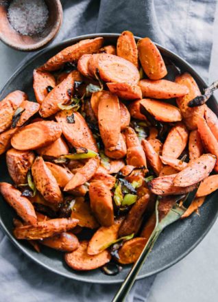 roasted carrots and leeks on a blue plate with a gold fork