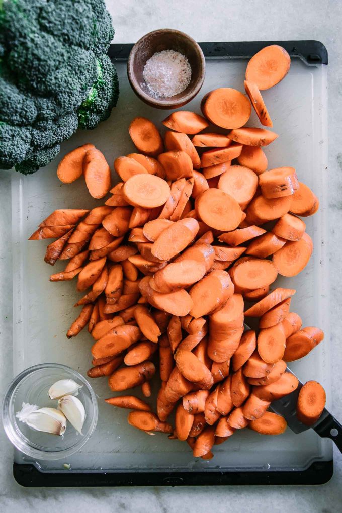 sliced carrots and a head of cauliflower on a white cutting board