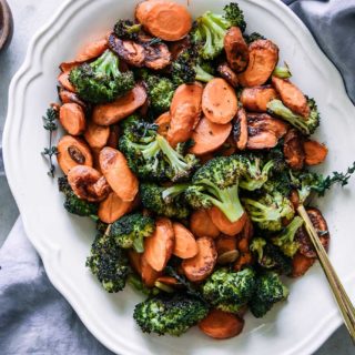roasted carrots and broccoli on a white plate with a blue napkin and a small bowl of salt