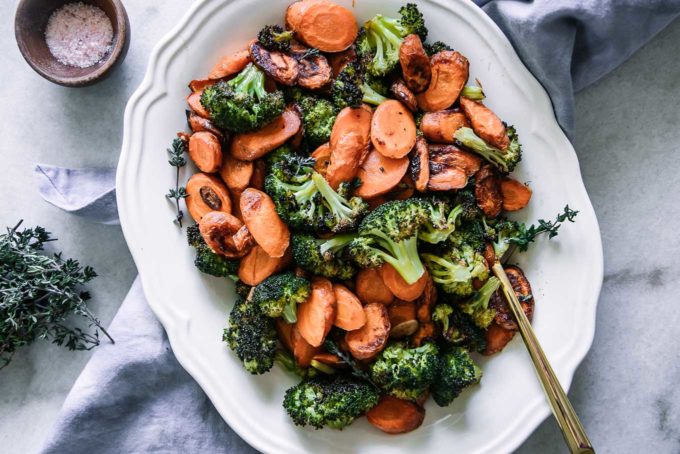roasted carrots and broccoli on a white plate with a blue napkin and a small bowl of salt