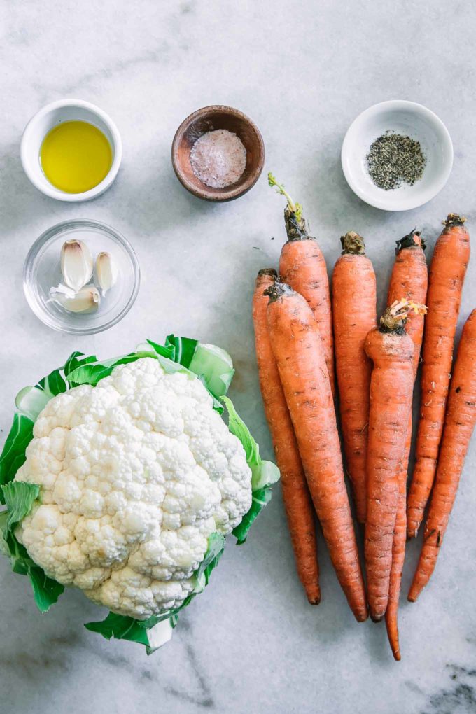 carrots, a head of cauliflower, and bowls of oil, garlic, salt, and pepper