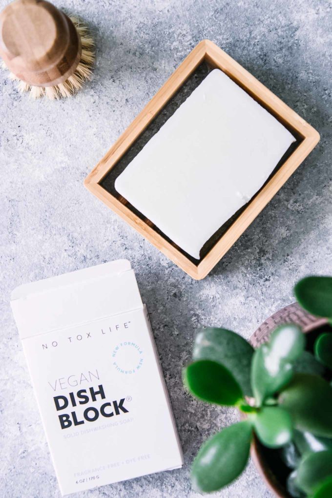 bar dish soap in a bamboo holder and a reusable wooden brush on a blue table