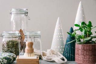 a reusable dish brush, glass food storage jars, and a reusable shopping bag on a table with holiday tree decorations