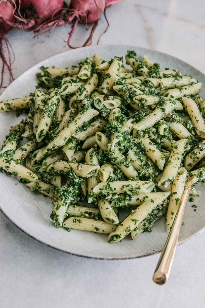 a plate of penne pasta with pesto sauce on a blue plate with red beets in the background