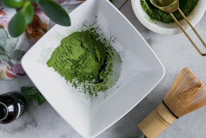 matcha green tea powder in a bowl with mint extract on a table with a wooden matcha whisk