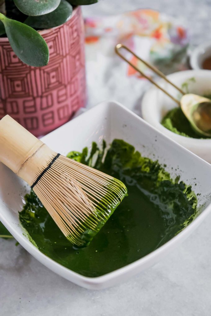 a bowl with matcha green tea powder dissolved in water and a wooden matcha whisk