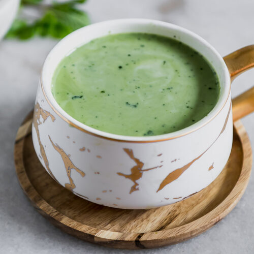 a mug of matcha green tea latte with a mint leaf and a sprinkle of green tea powder on top