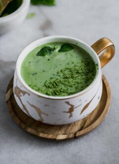 a green tea matcha latte in a white ceramic mug on a wooden saucer