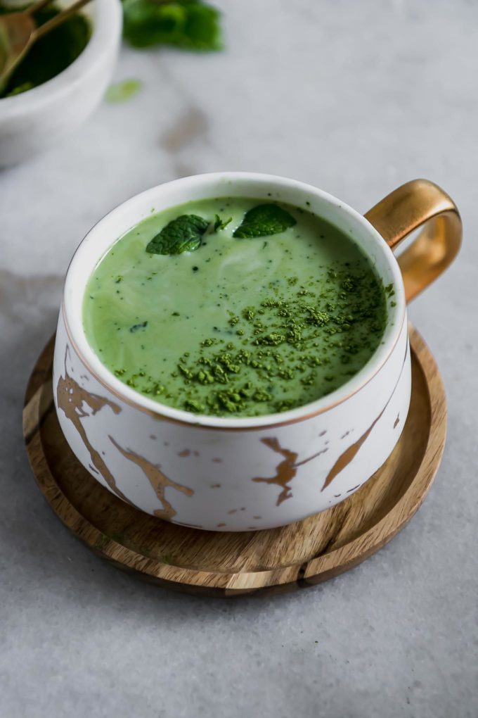 a green tea matcha latte in a white ceramic mug on a wooden saucer