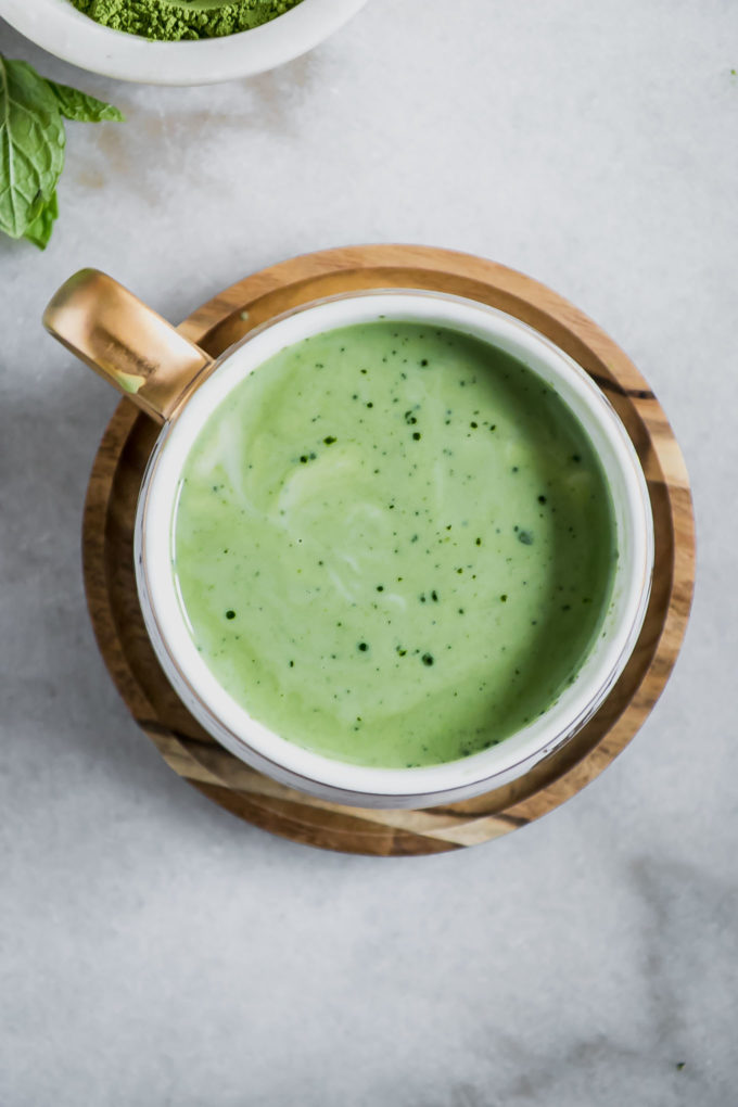 green tea latte inside a white cup on a wooden saucer