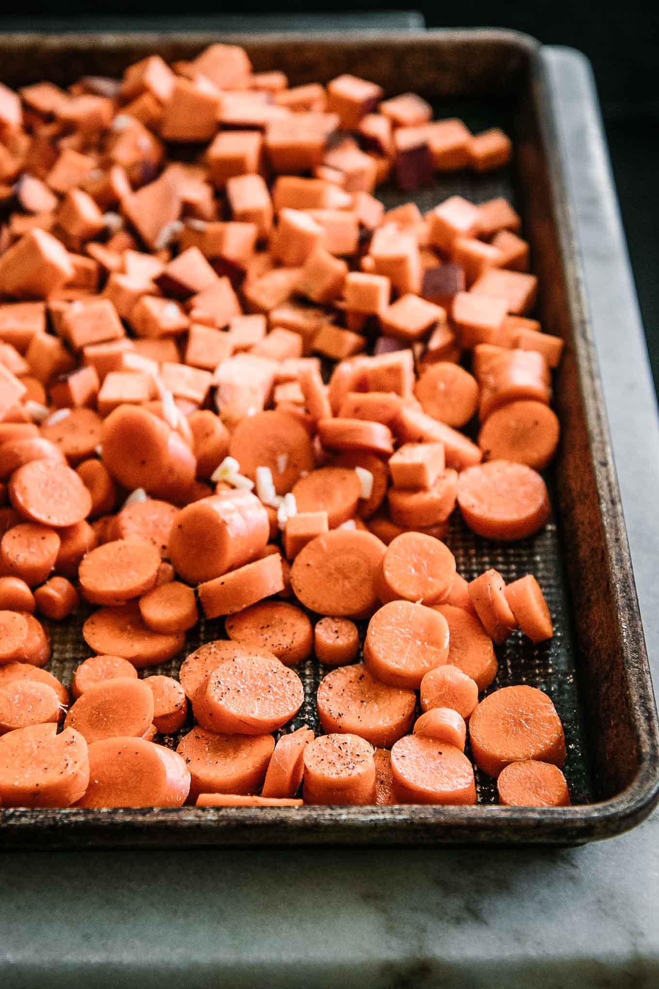 sliced carrots and cut sweet potatoes on a baking sheet