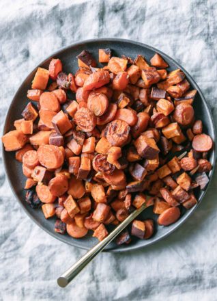roasted sweet potatoes and carrots on a blue plate with a gold fork on a white tablecloth
