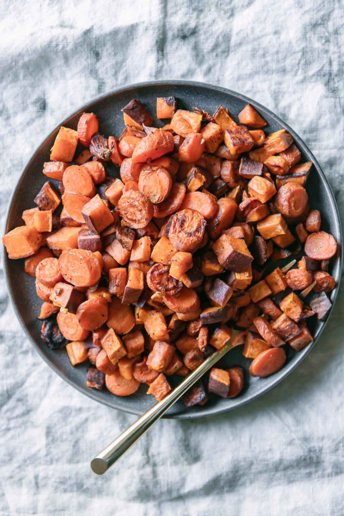 roasted sweet potatoes and carrots on a blue plate with a gold fork on a white tablecloth