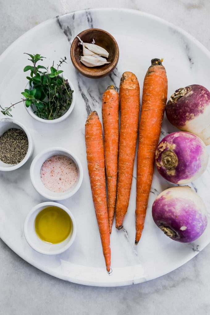 a marble plate with carrots, turnips, and bowls of oil, herbs, garlic, salt, and pepper