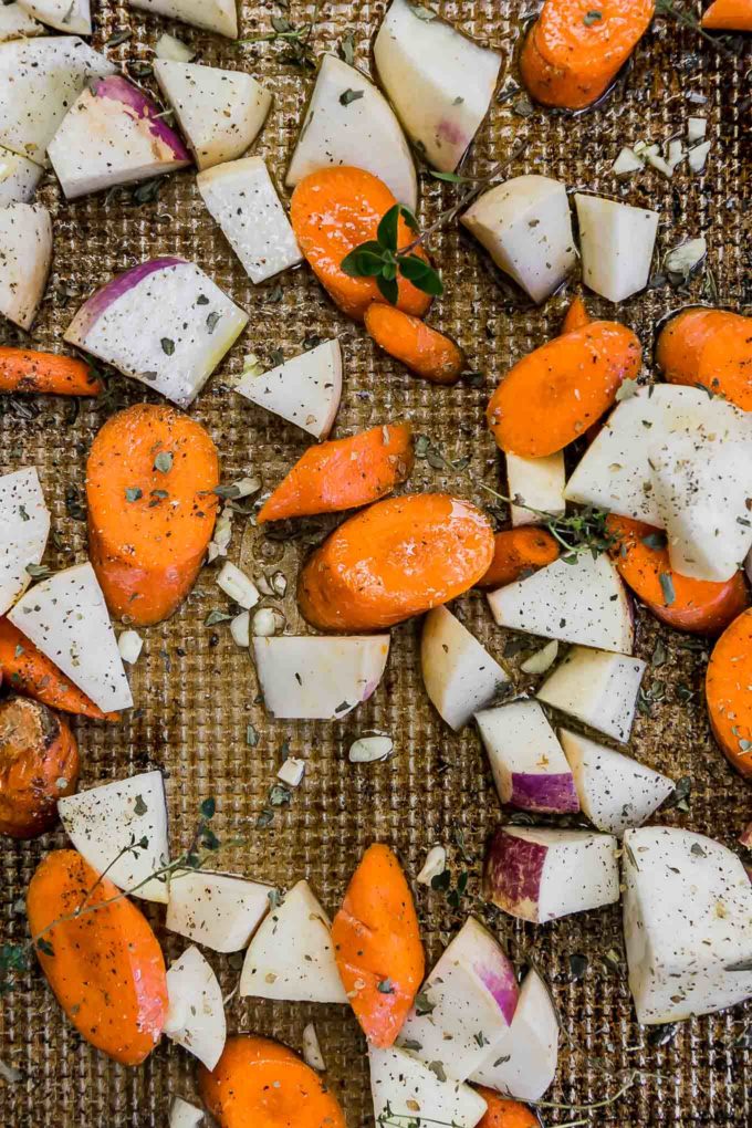 sliced carrots and turnips on a sheet pan with garlic and fresh herbs