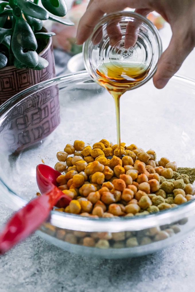 a hand pouring maple syrup into a bowl of chickpeas