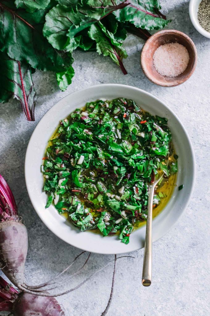 a bowl of green herb sauce with a gold fork on a blue table