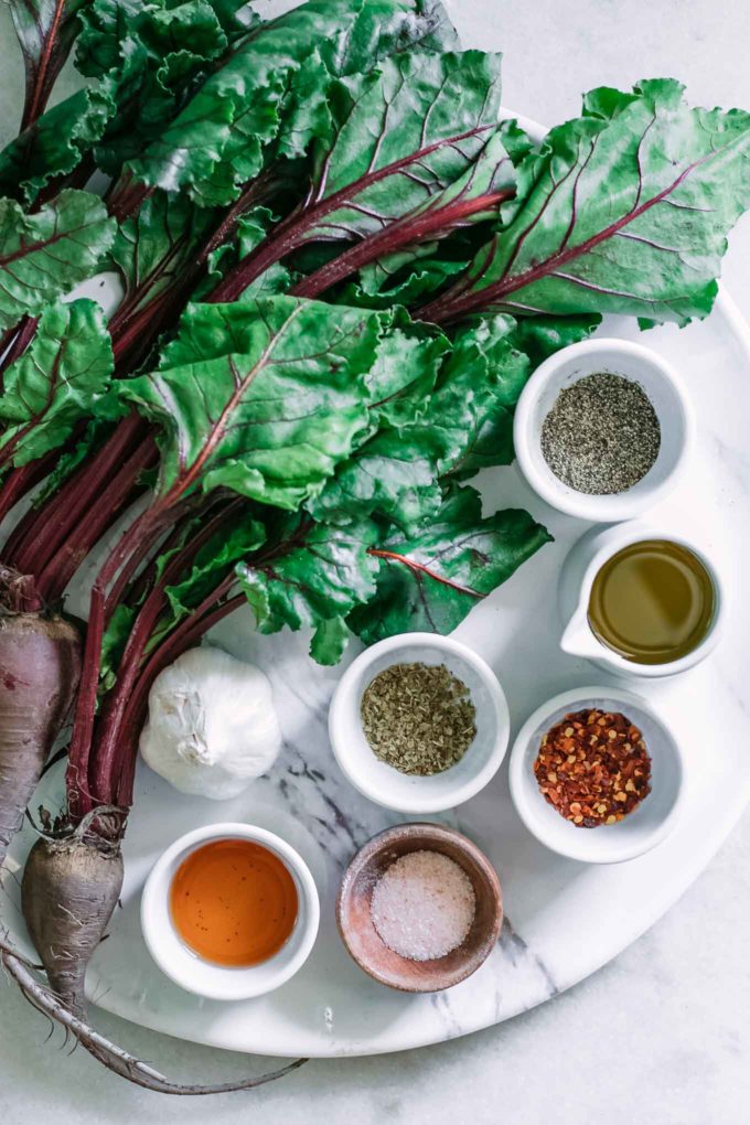 beet greens and bowls of olive oil, garlic, red wine vinegar, salt, and pepper on a white table