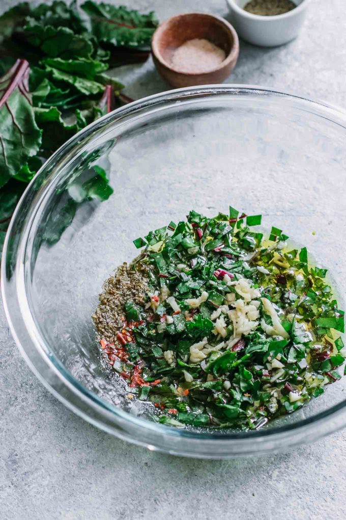 chopped herbs, greens, garlic, and red pepper in a glass mixing bowl
