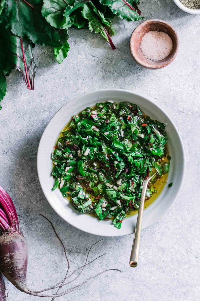 a bowl of chimichurri with a gold fork on a blue table