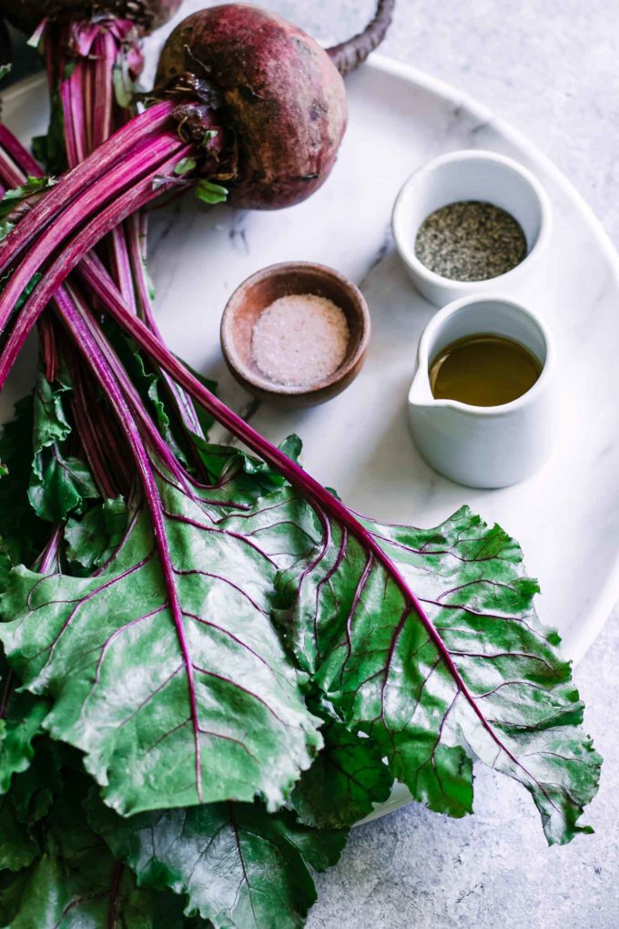 beets with greens and bowls of salt, pepper, and oil on a white table