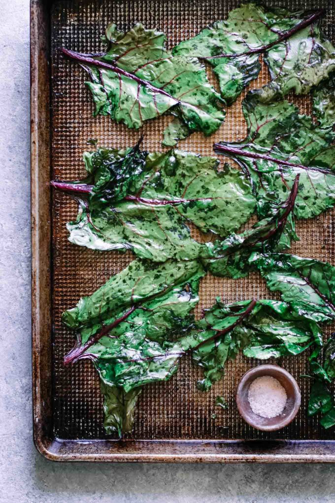 roasted beet greens on a baking sheet with a bowl of salt