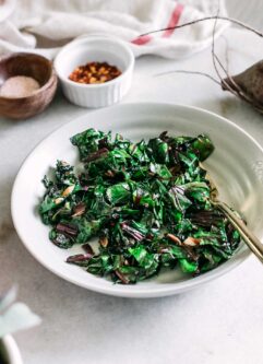 sauteed beet leaves in a white bowl with a gold fork on a white table