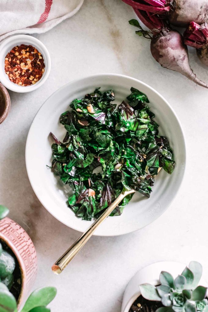 cooked beet leaves in a small side dish on a table with beets and flowers