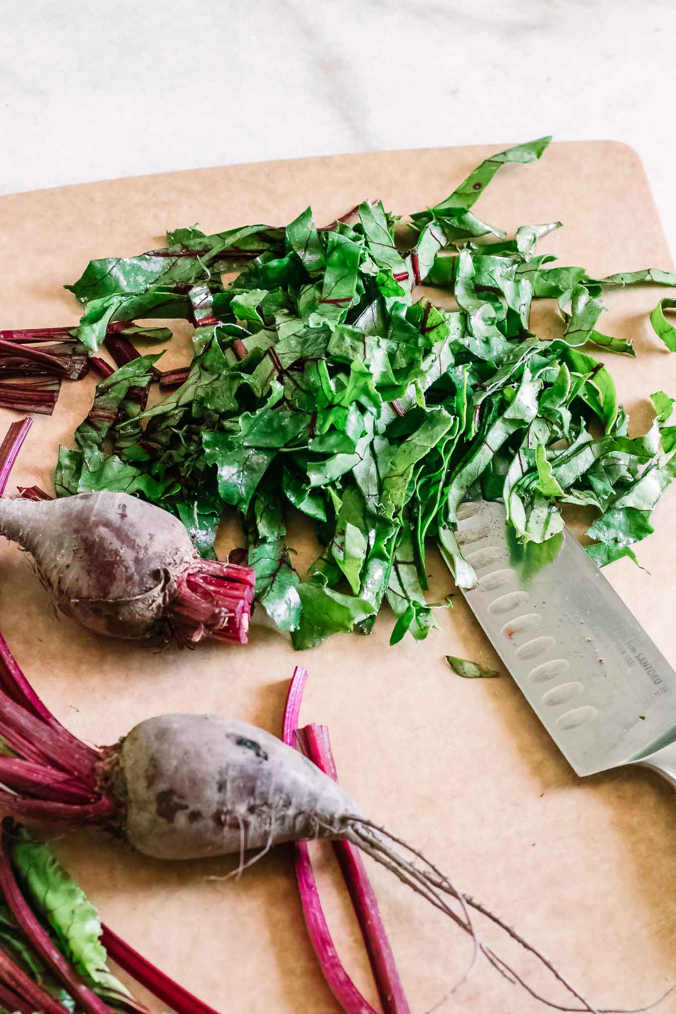 chopped beet greens and red beet roots on a brown cutting board