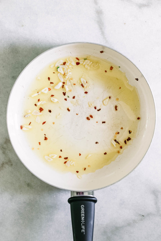 a pan with olive oil, garlic, and red pepper on a marble countertop