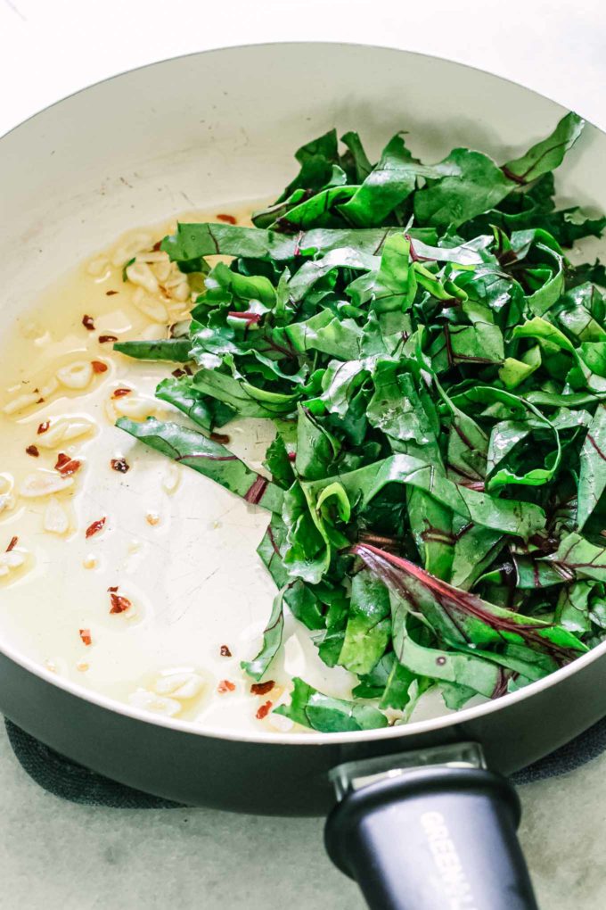 chopped beet greens in a pan with olive oil, garlic, and red pepper