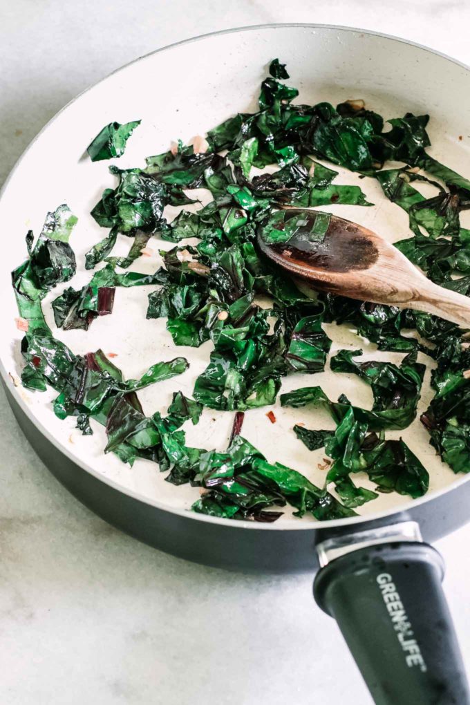 wilted beet greens in a white pan with a wooden spoon
