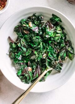 beet greens in a white bowl with a gold fork