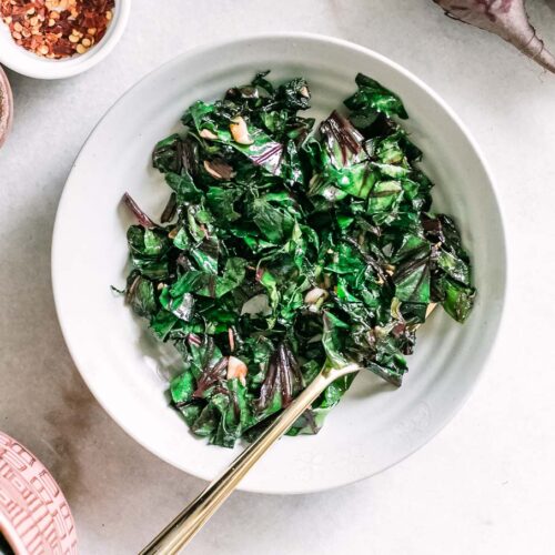 beet greens in a white bowl with a gold fork