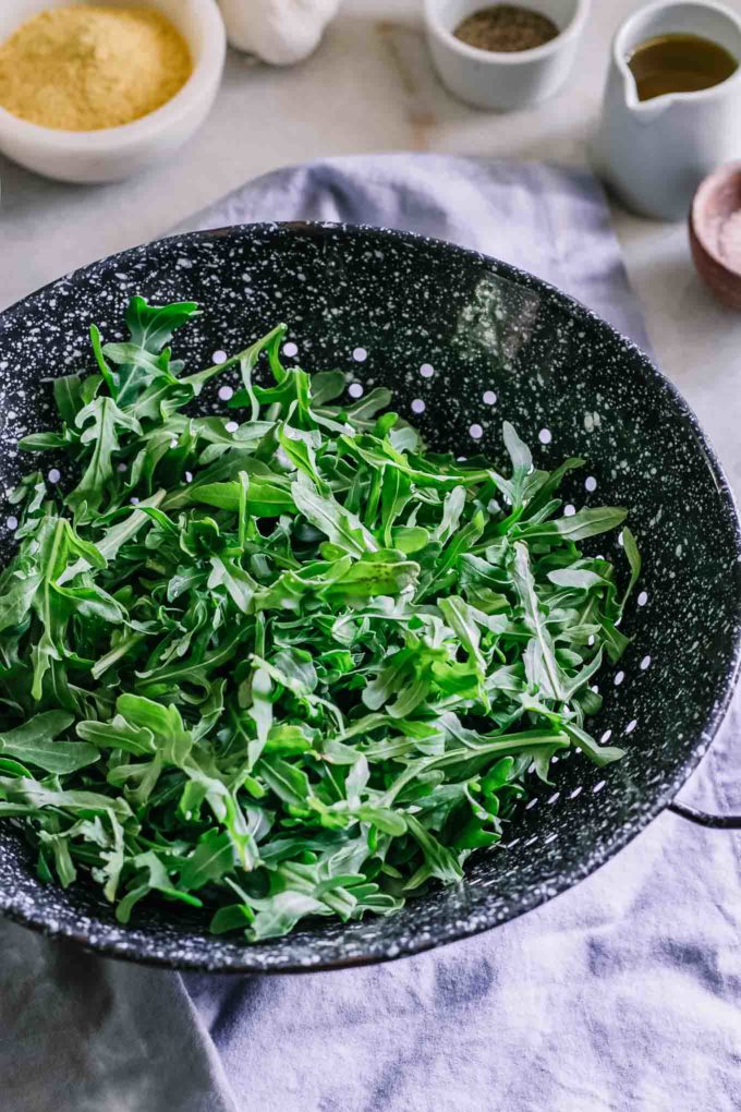 a colander with arugula on a blue table