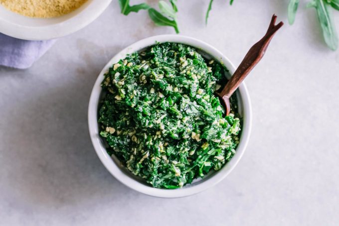 a bowl of arugula pesto with a wooden spoon on a white table