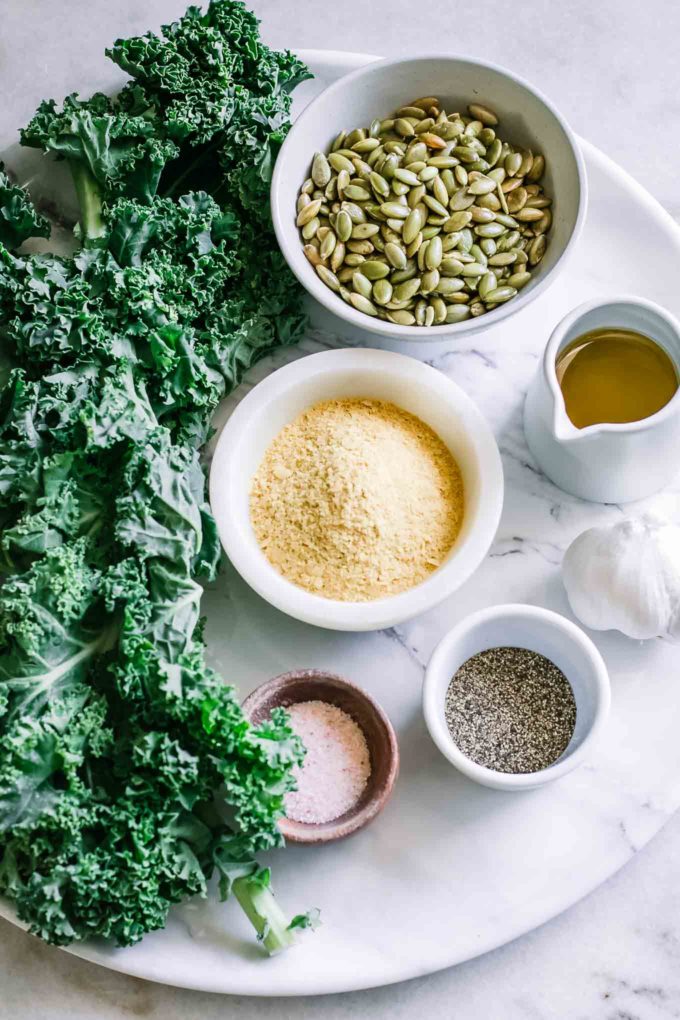 a bunch of kale and bowls of nuts, nutritional yeast, olive oil, garlic, salt, and pepper