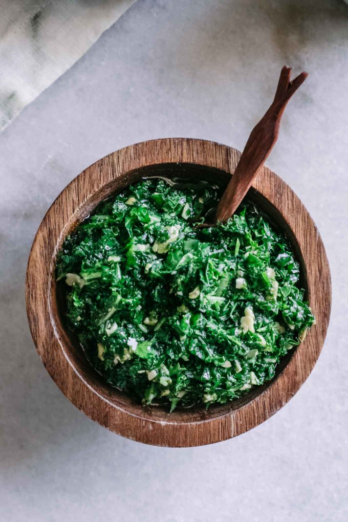 a close up of pesto sauce made from kale in a wooden bowl with a small wooden spoon