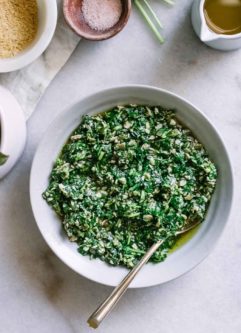 parsley pesto sauce in a blue bowl with a gold fork on a white table