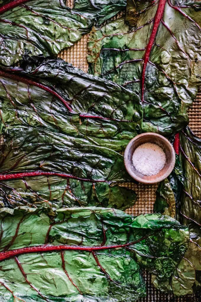 roasted chard chips on a sheet pan with a bowl of salt