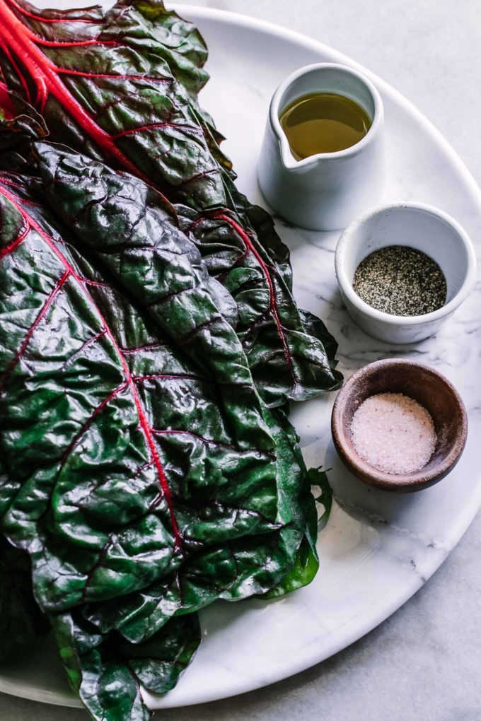 chard leaves and bowls of olive oil, salt, and pepper on a white table