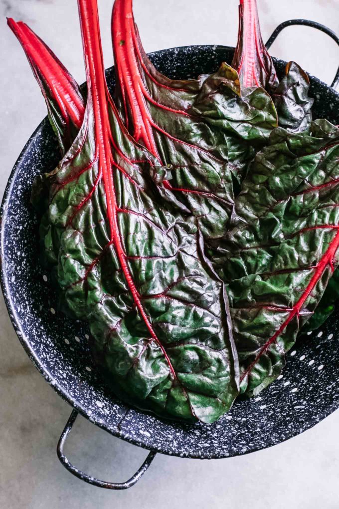 washed chard leaves in a blue colander on a white table