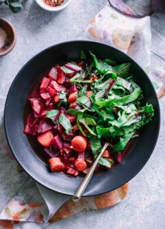 beet vegetable soup with chopped beet greens in a black bowl on a blue table